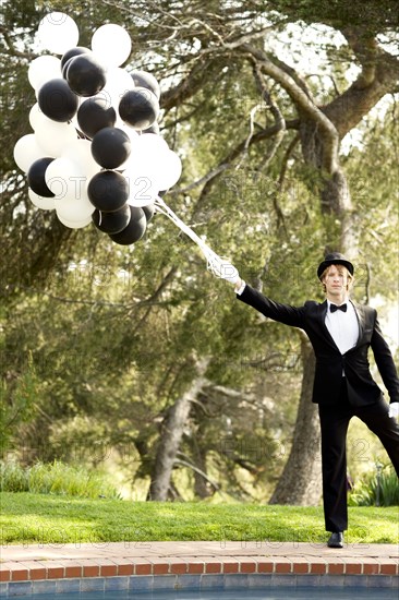 Caucasian man in tuxedo holding bunch of balloons