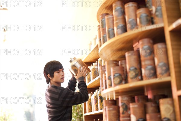 Mixed race man lifting canister from shelf in shop