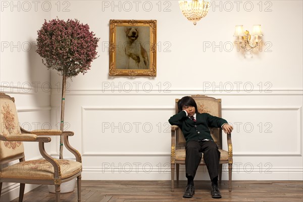 Frustrated Vietnamese boy sitting on elegant chair