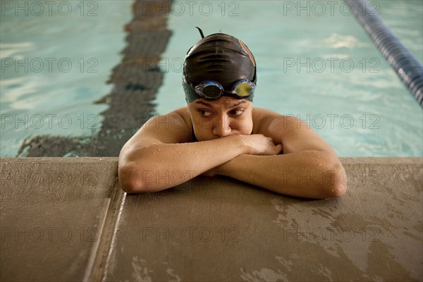 Unhappy Pacific Islander swimmer leaning at edge of pool