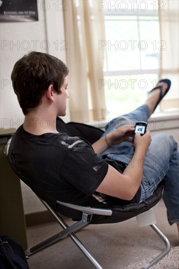 Caucasian man text messaging on cell phone in dorm room