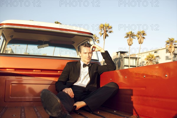 Serious Caucasian man sitting in tuxedo in back of truck