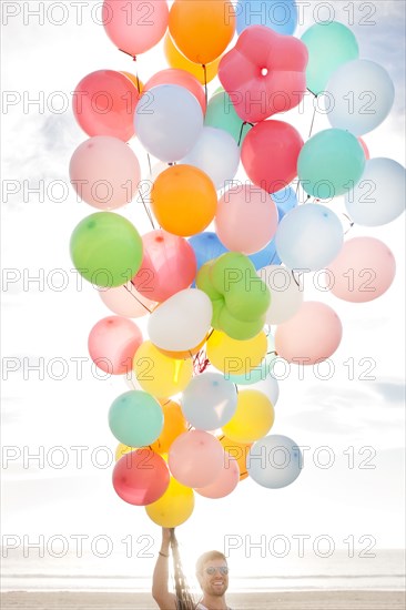 Caucasian man holding balloons on beach