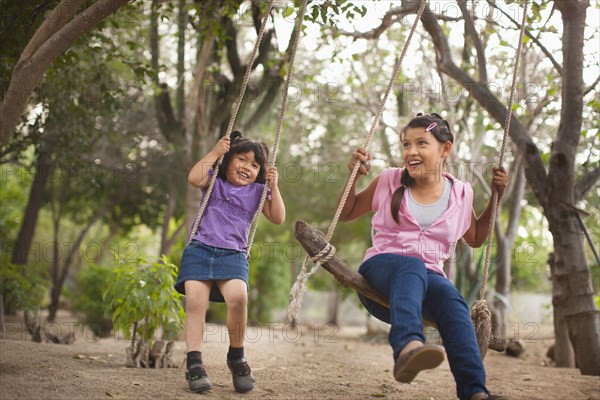 Hispanic sisters swinging on swings