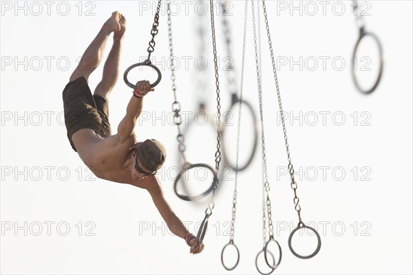 Mixed race man swinging on athletic rings