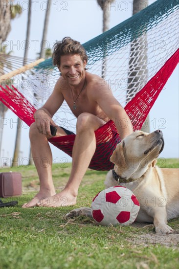 Caucasian man relaxing in hammock petting dog