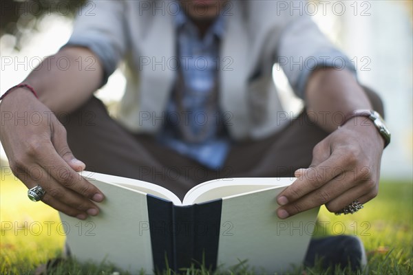 Hispanic man reading book in grass