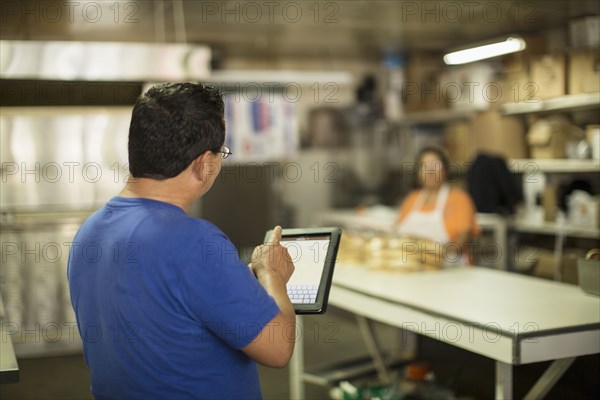 Hispanic baker using tablet computer in kitchen