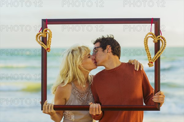 Caucasian couple holding frame with hearts and kissing