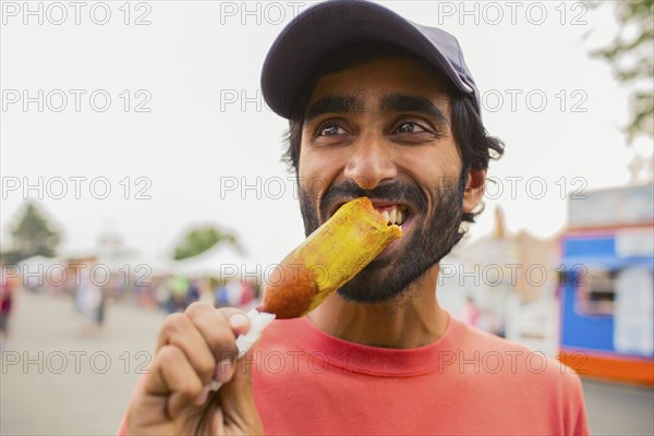 Asian man eating corn dog outdoors