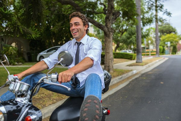 Hispanic businessman driving moped on neighborhood road