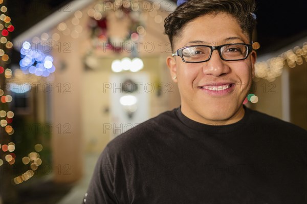 Hispanic man smiling outside house decorated with string lights