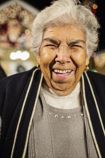 Older Hispanic woman smiling outside house decorated with string lights