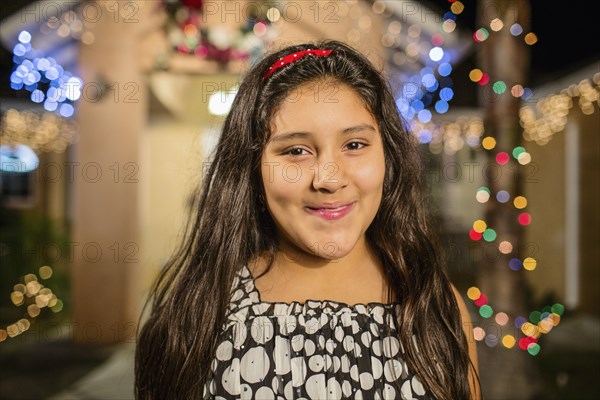 Hispanic girl smiling outside house decorated with string lights