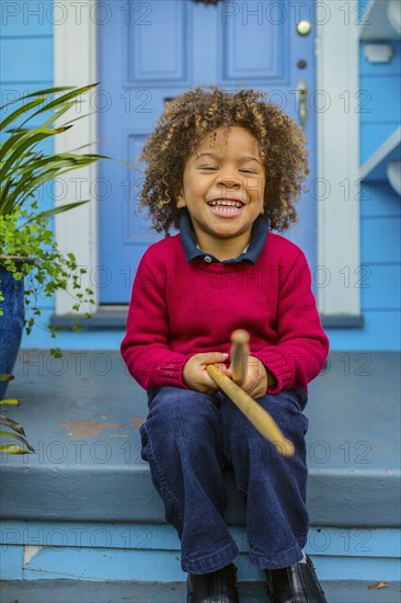 Pacific Islander boy with drumsticks sitting on front stoop