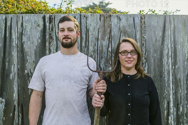 Caucasian couple holding pitchfork near fence