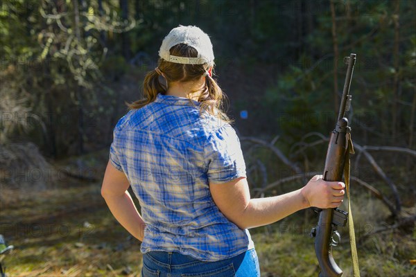 Caucasian woman carrying rifle in forest