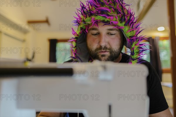 Caucasian man wearing fuzzy hat using sewing machine