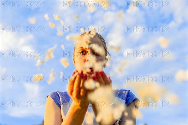 Caucasian teenage girl blowing flower petals under blue sky