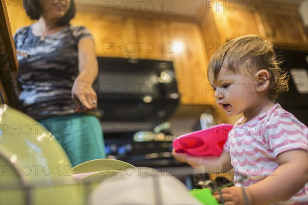 Baby girl helping mother load dishwasher