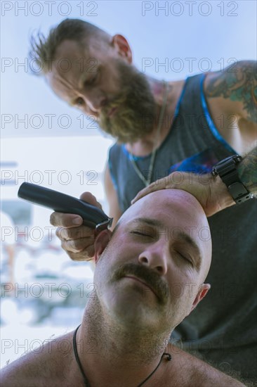 Caucasian man shaving head of friend