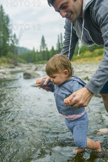 Father helping daughter walk in river