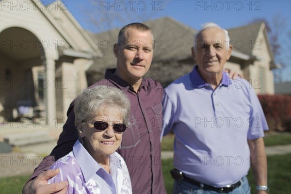 Older Caucasian parents and son smiling in yard