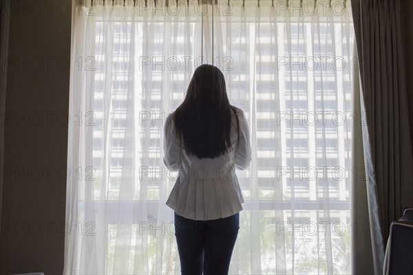 Asian teenage girl standing at hotel window