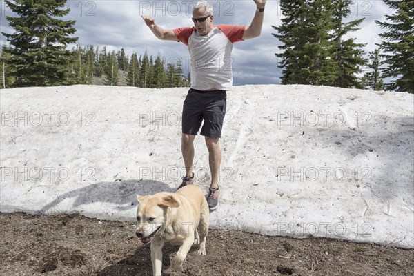 Caucasian man wearing shorts sliding on snow with dog