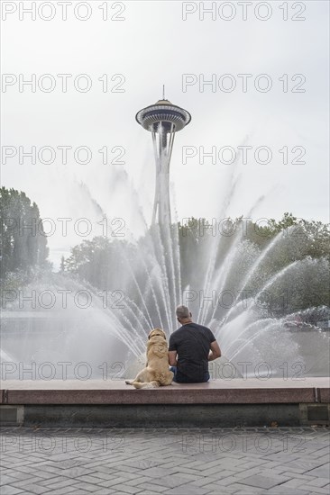 Caucasian man and dog sitting on fountain near tower