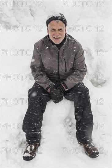 Smiling Caucasian man sitting on pile of snow