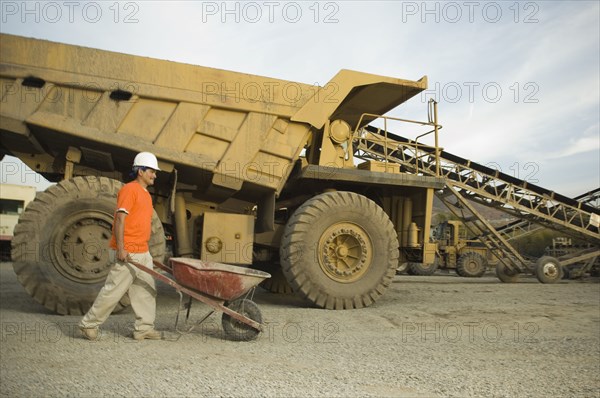 Hispanic man pushing wheelbarrow at gravel plant