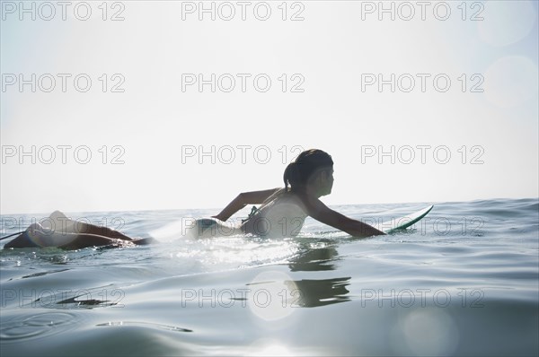 Hispanic girl paddling on surfboard