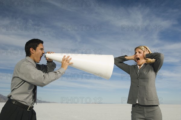 Hispanic businessman yelling at businesswoman through megaphone