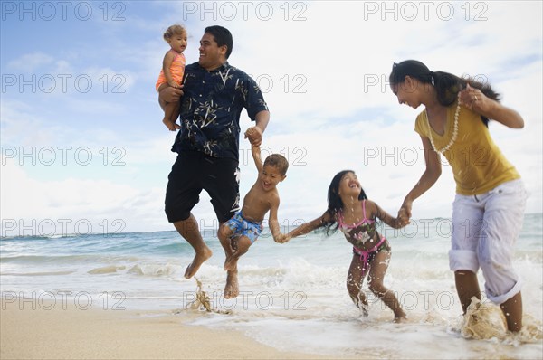 Pacific Islander family jumping in ocean surf