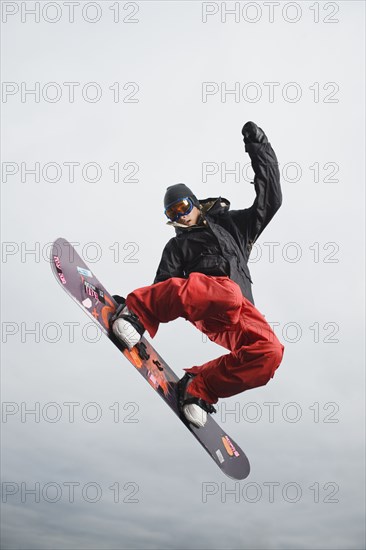 Mixed race teenager in mid-air on snowboard