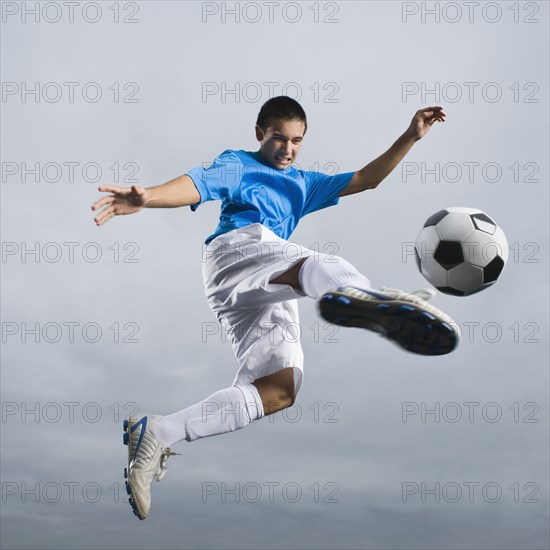 Mixed race teenager in mid-air kicking soccer ball