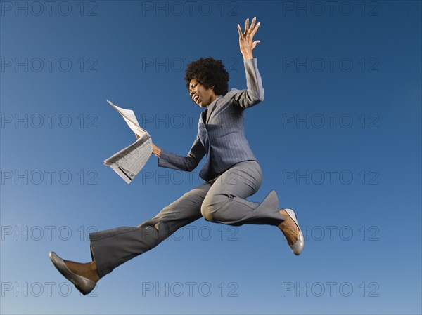 African businesswoman reading newspaper in mid-air