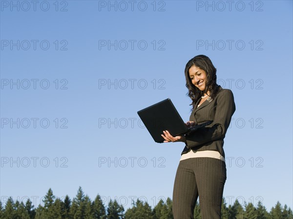 Mixed race businesswoman using laptop outdoors