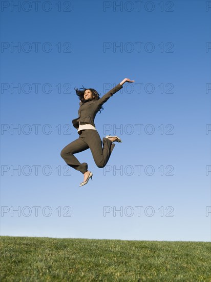 Mixed race businesswoman jumping in field