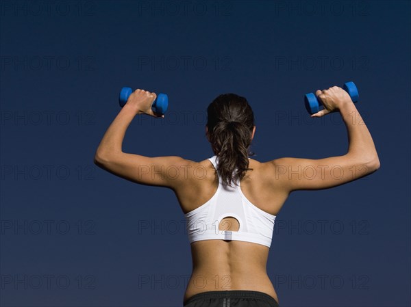 Rear view of mixed race woman doing shoulder presses with dumbbells