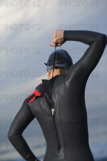 Hispanic woman zipping wetsuit on beach