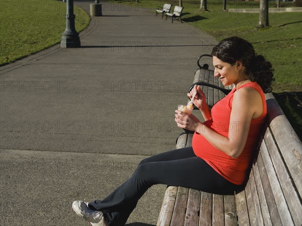 Pregnant Middle Eastern woman eating fruit in park