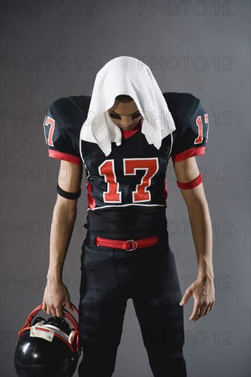 Mixed race football player looking down with towel on head