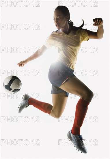 Mixed race soccer player kicking soccer ball in mid-air