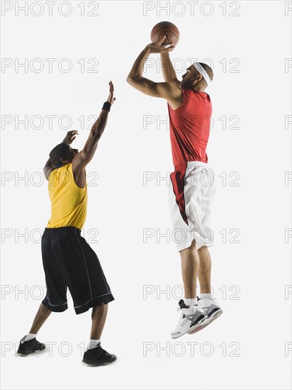 African man shooting basketball over opponent