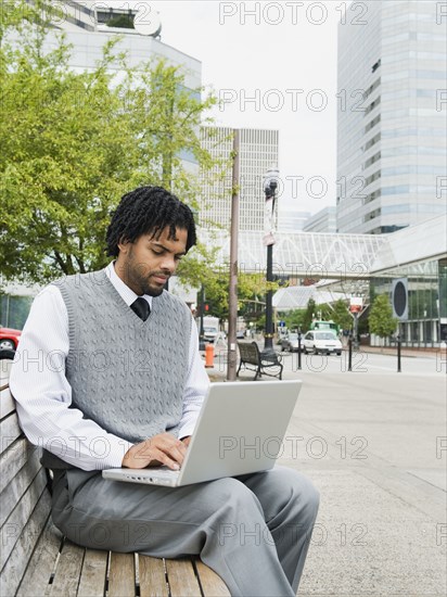 Mixed race businessman using laptop on city bench