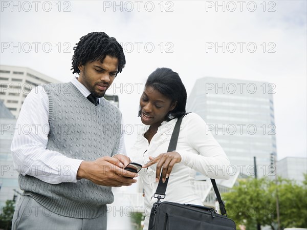 Businessman and businesswoman looking at cell phone in city