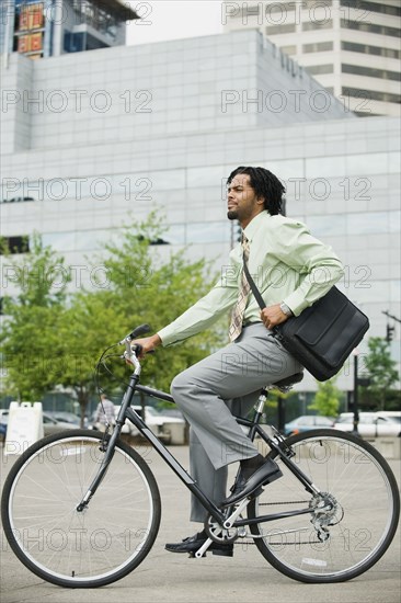 Mixed race businessman riding bicycle in city