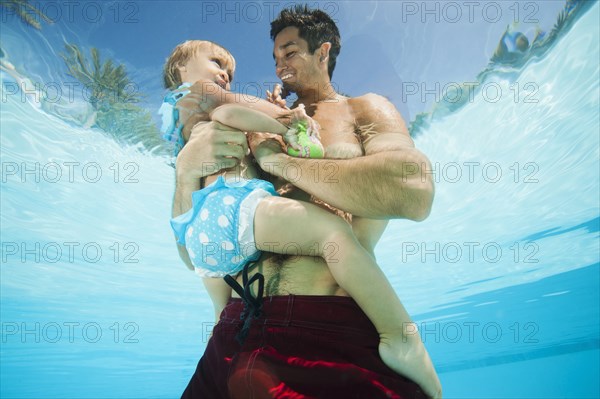 Mixed race father holding daughter in swimming pool